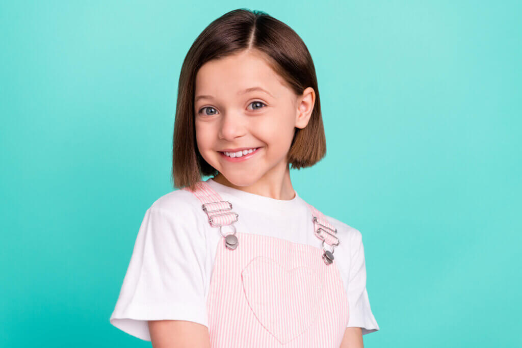 Menina de cabelo curto sorrindo em frente a um fundo verde